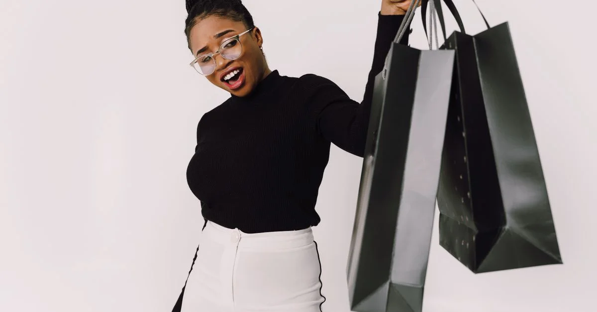 Femme souriante avec des lunettes tenant joyeusement des sacs de shopping sur un fond blanc.
