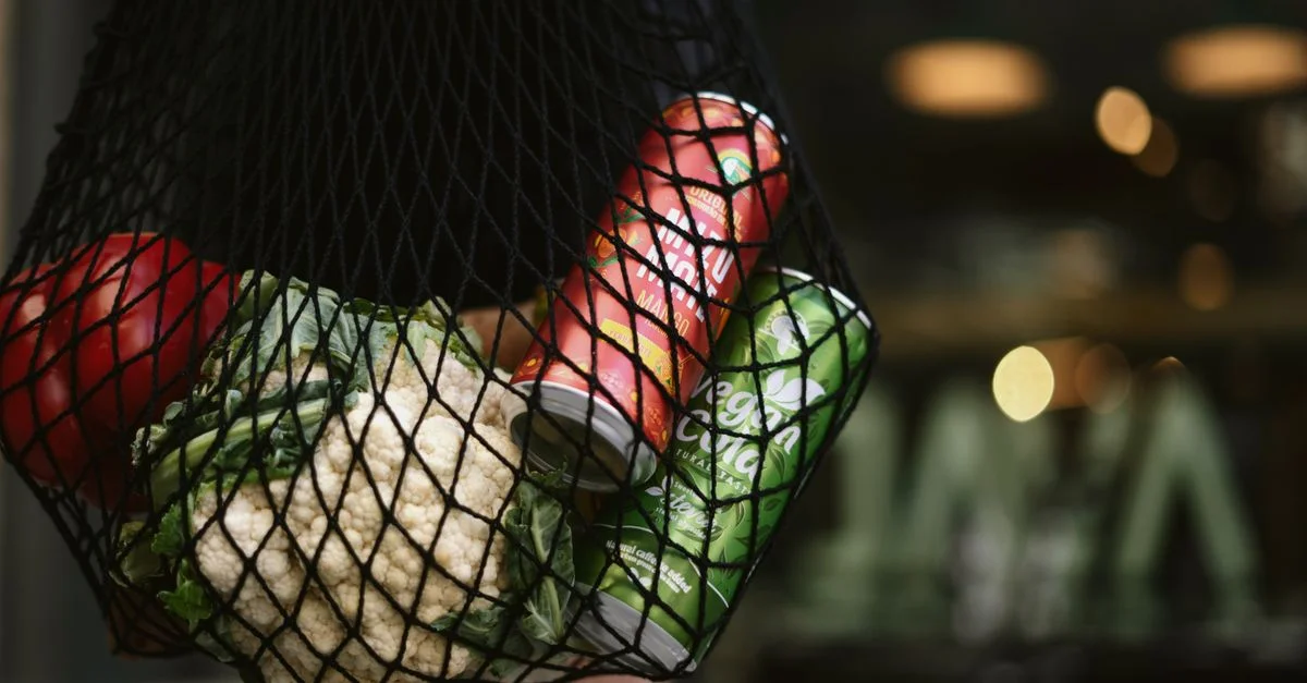Un sac en maille contenant des légumes frais et des boissons en conserve dans un cadre urbain, mettant en avant des achats éco-responsables.