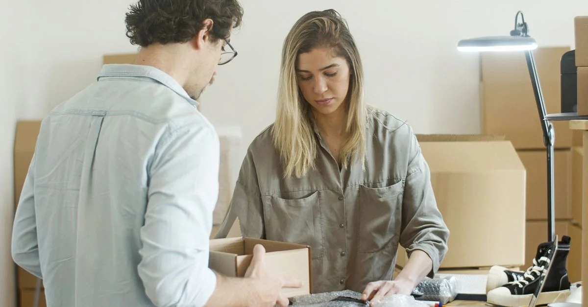 Deux jeunes adultes emballant des vêtements dans un bureau pour leur startup de boutique en ligne.