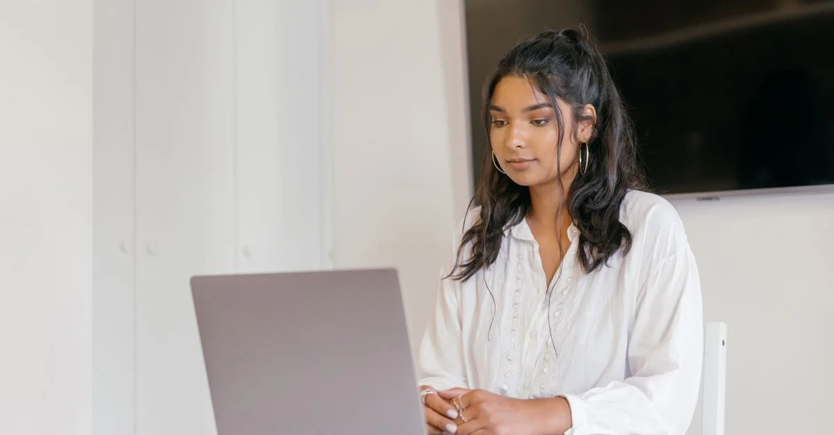 Une jeune femme concentrée sur ses études avec son ordinateur portable dans un cadre intérieur moderne.
