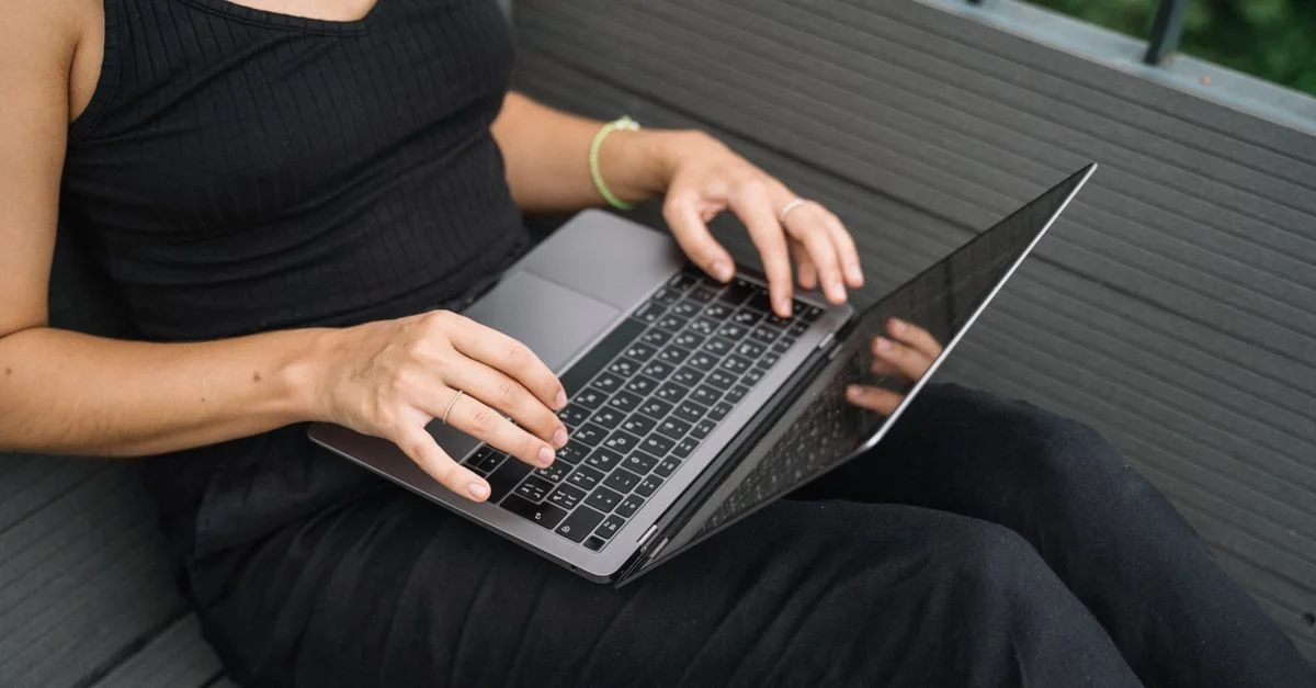 Gros plan sur une femme tapant sur un ordinateur portable assise en plein air sur une terrasse en bois.