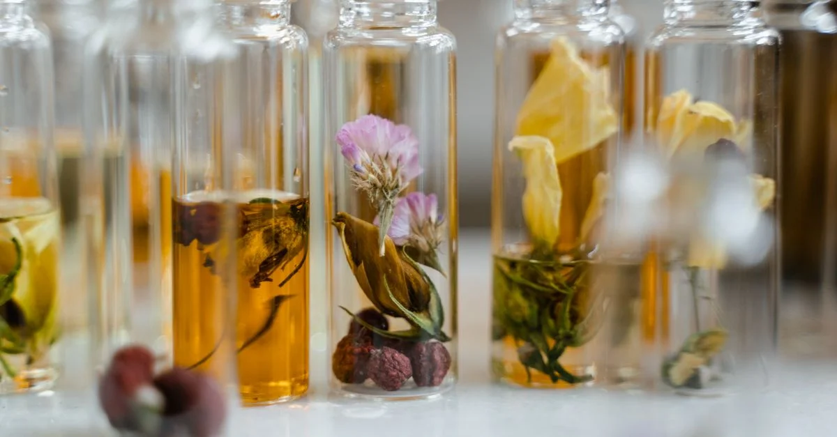 Gros plan sur un assortiment de fleurs sèches immergées dans des flacons en verre, idéal pour les produits de parfum naturel.