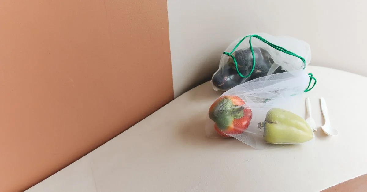 Des poivrons colorés dans un sac en maille réutilisable sur un fond minimaliste, promouvant un style de vie écologique.